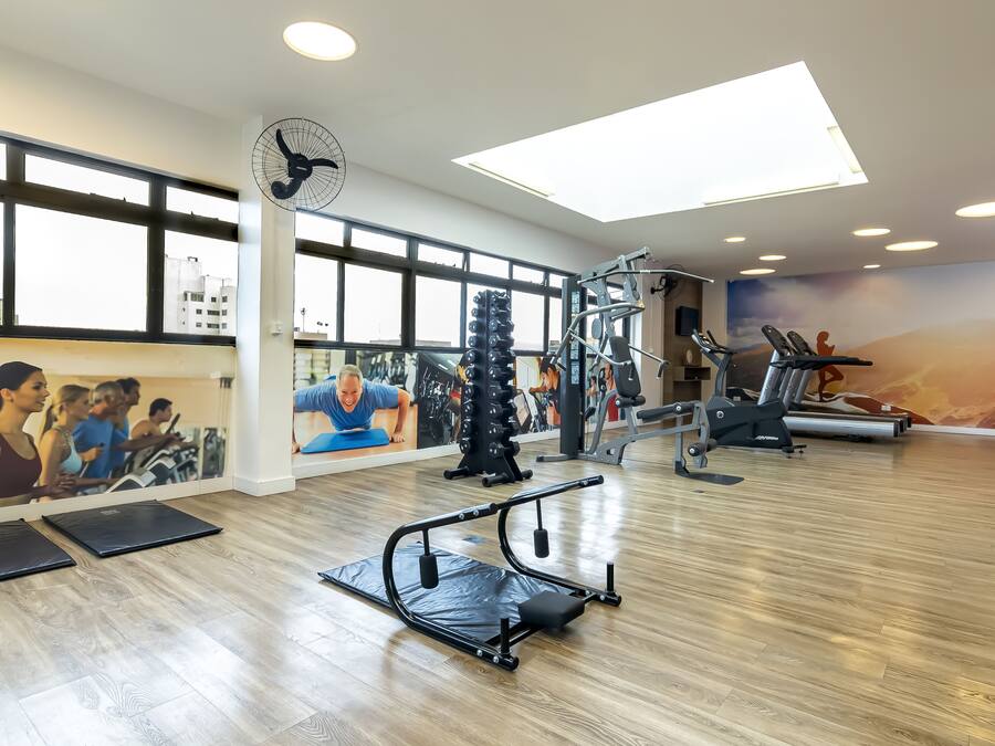 Un gimnasio con equipamiento de ejercicio, ventanas amplias y un mural.