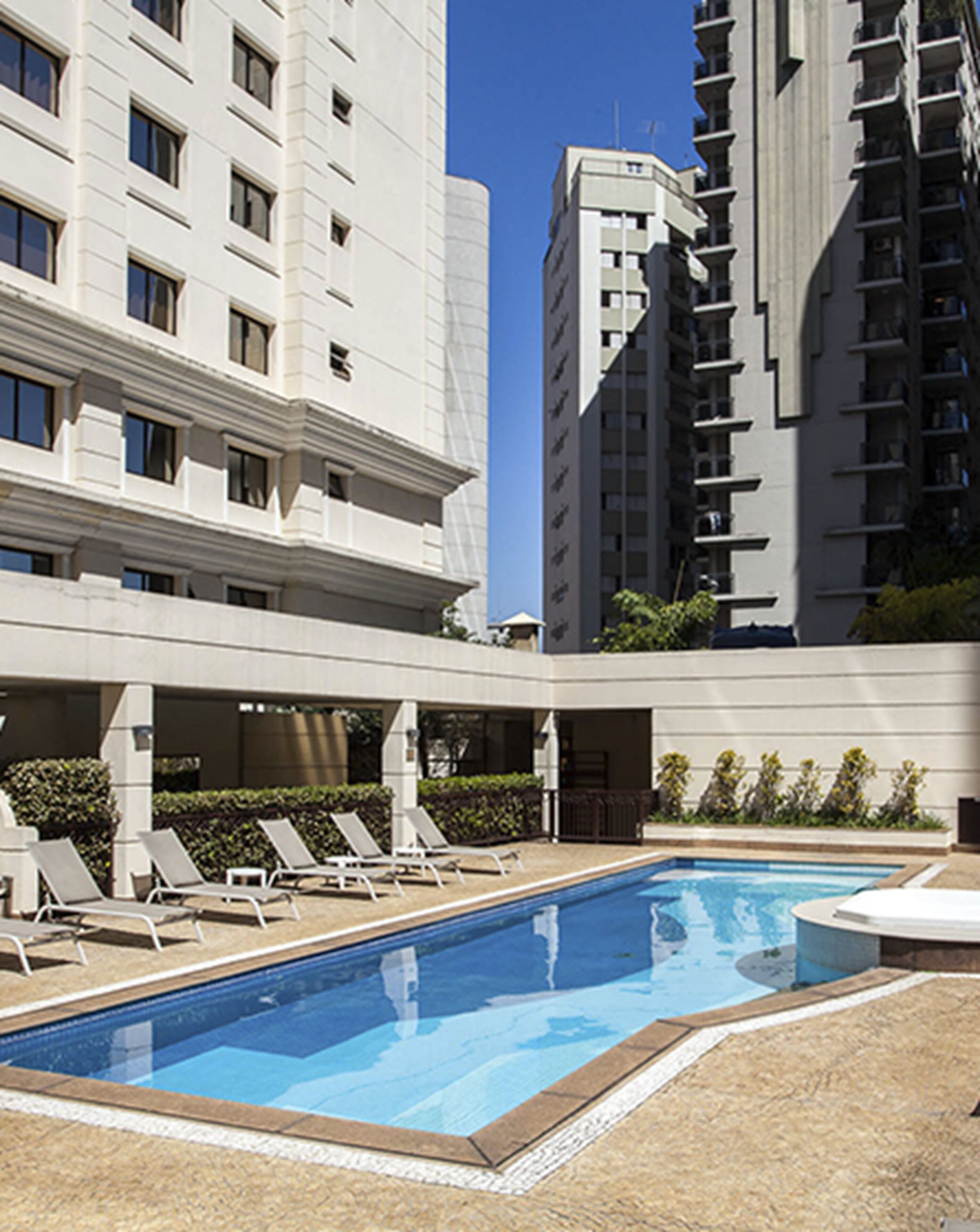 A swimming pool with lounge chairs, surrounded by a building with multiple floors and balconies.