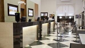 Zona de recepción de un hotel con mostrador de registro, pantalla digital y escritorio.