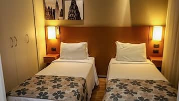 Habitación de hotel con dos camas individuales, cada una con una colcha estampada con motivos florales y almohadas blancas. Hay dos mesitas de noche con lámparas, y las paredes están decoradas con cuadros enmarcados.