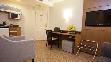 A compact hotel room with a kitchenette, a desk with a laptop, a TV, and two chairs.