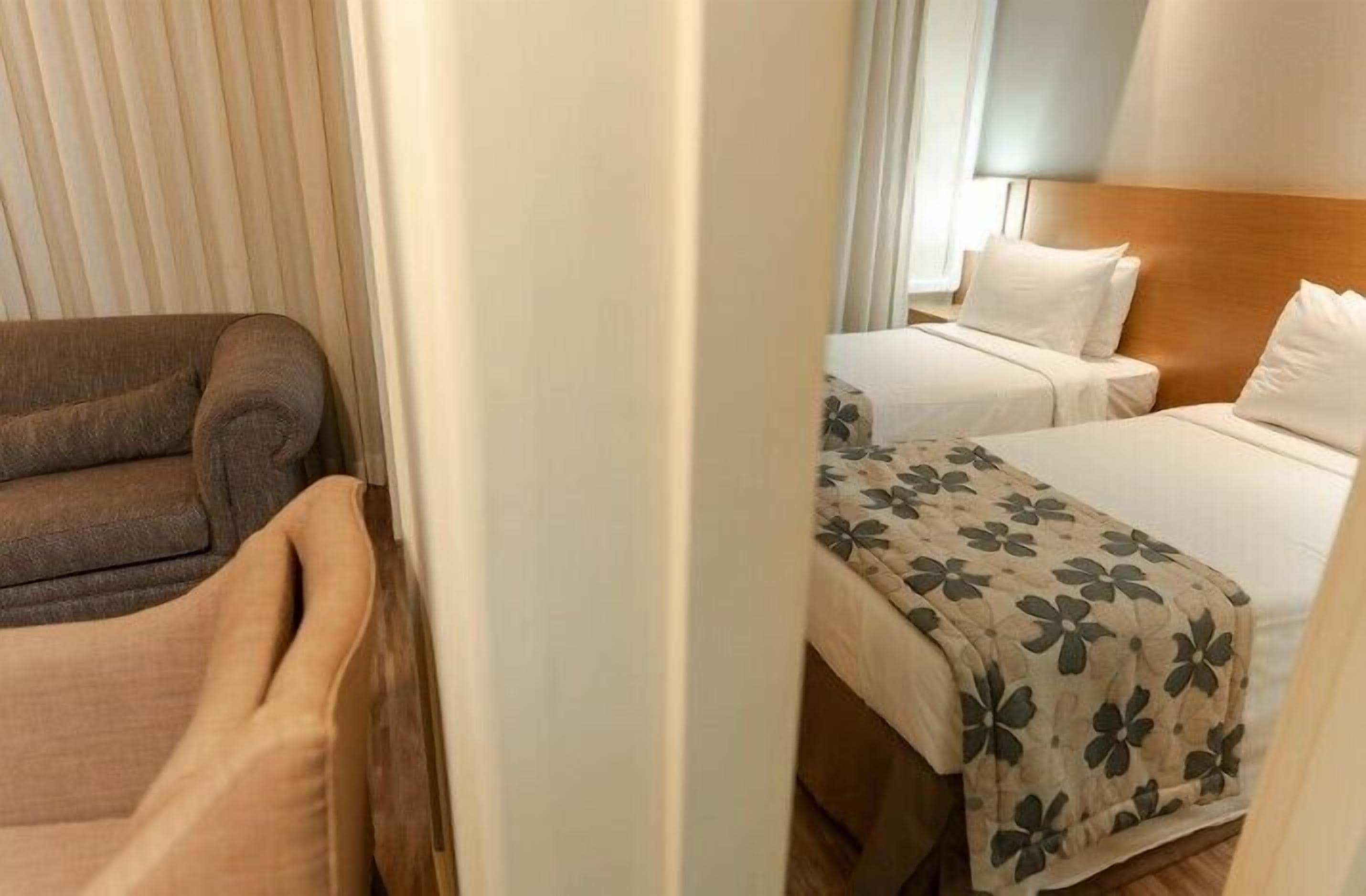 A hotel room with a sofa, two beds with floral bedspreads, and a wooden headboard.