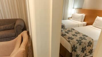 A hotel room with a sofa, two beds with floral bedspreads, and a wooden headboard.