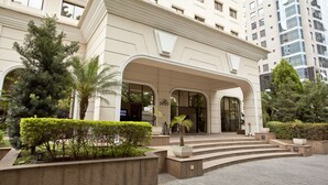 Una entrada de hotel moderna con un arco imponente, un jardín cuidado y una vista de un edificio alto al fondo.