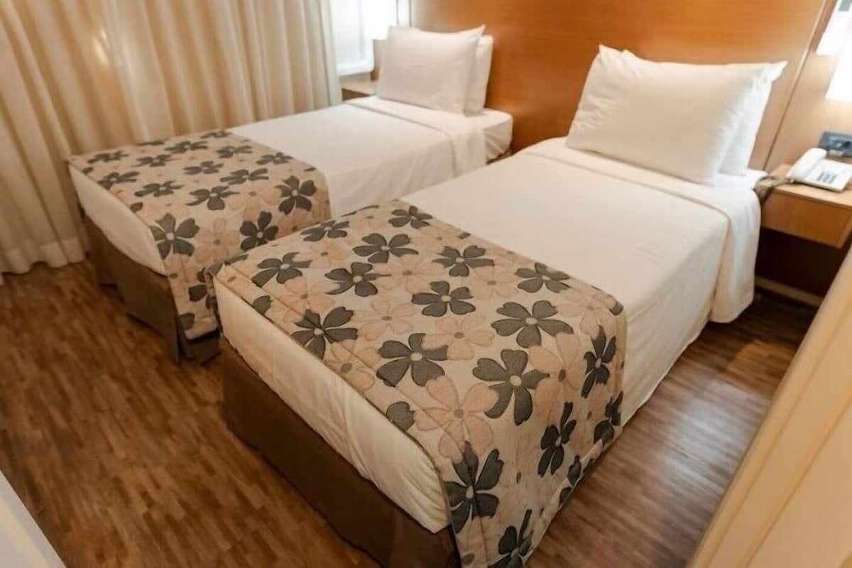 Two single beds with floral bedspreads, a wooden headboard, a nightstand with a phone, and a window with curtains.