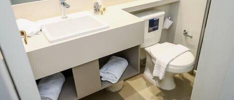 A modern bathroom with a white sink, two faucets, a toilet, and a towel rack.
