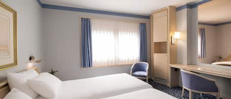 Quarto de hotel com duas camas, uma escrivaninha, uma cadeira, uma janela ampla com cortinas e um espelho.