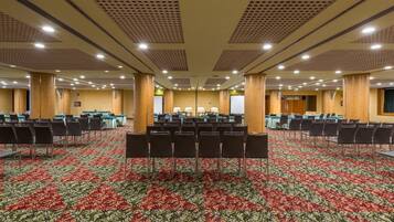 Un salón de conferencias con filas de sillas, suelo alfombrado e iluminación empotrada en el techo.