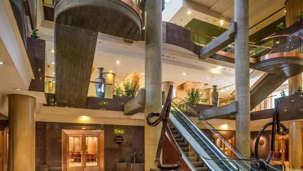 En modern hotellobby med en central trappa, flera våningsplan och en reception.