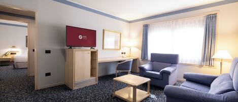 Una habitación de hotel con televisión, escritorio, dos sillas, sofá y ventana con cortinas.