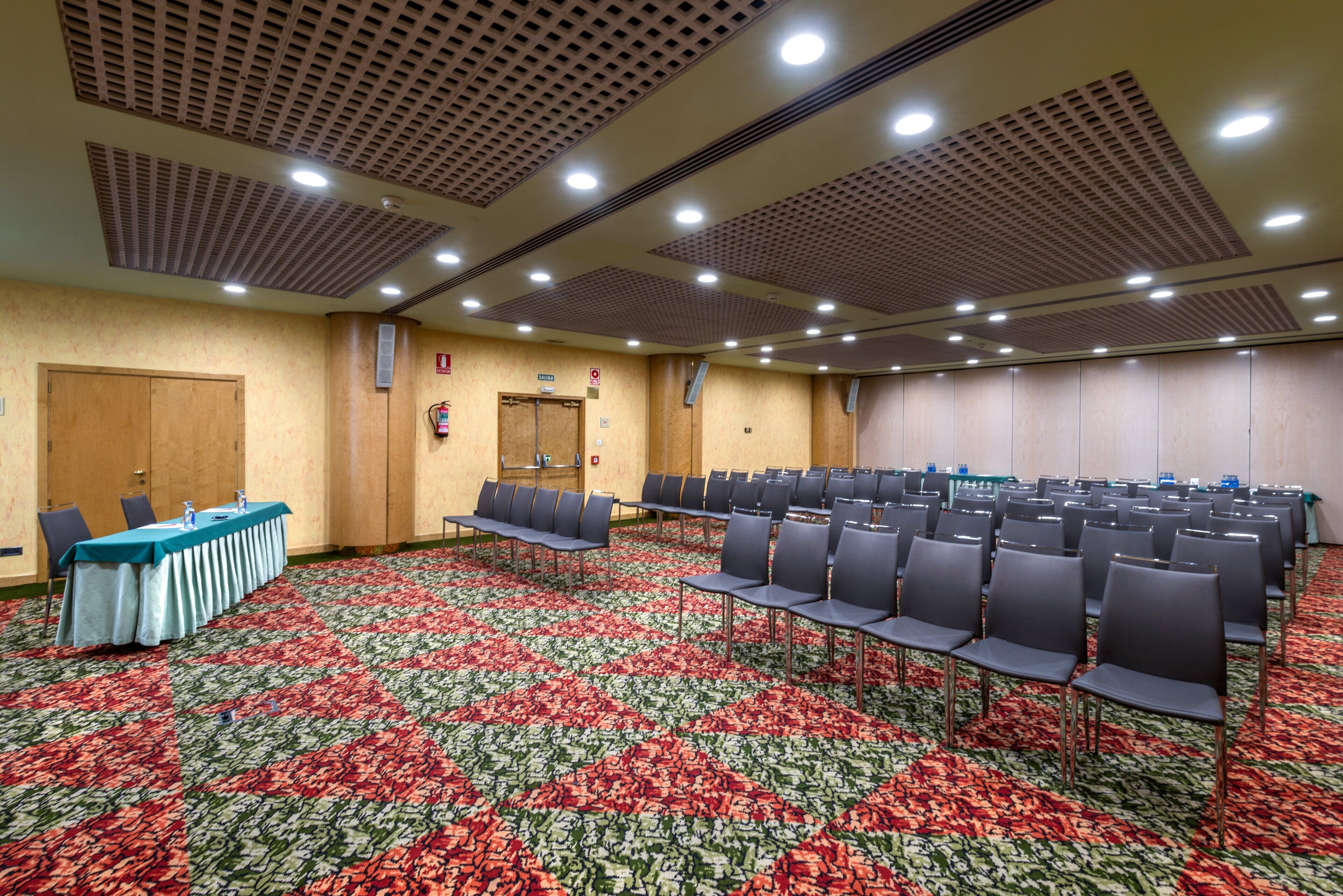 A conference room with rows of chairs, a table with water bottles, and a patterned carpet.
