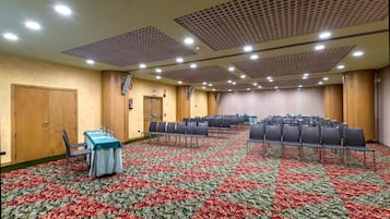 A conference room with a patterned carpet, rows of chairs, a table with a tablecloth, and a door.