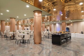 Un amplio comedor con varias mesas y sillas, pilares grandes y un mostrador tipo bufé.