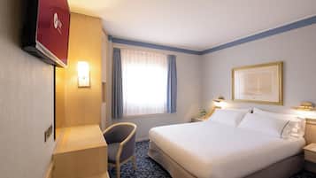Une chambre d’hôtel avec un lit, un bureau, une chaise, une télévision et une fenêtre avec des rideaux.