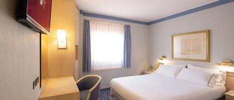 A hotel room with a bed, a desk, a chair, a TV, and a window with curtains.