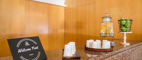 Un espace d’accueil avec un panneau indiquant un « point d’information », un coin café avec des tasses et un plateau, un bocal en verre rempli de citrons et un panier de pommes vertes.