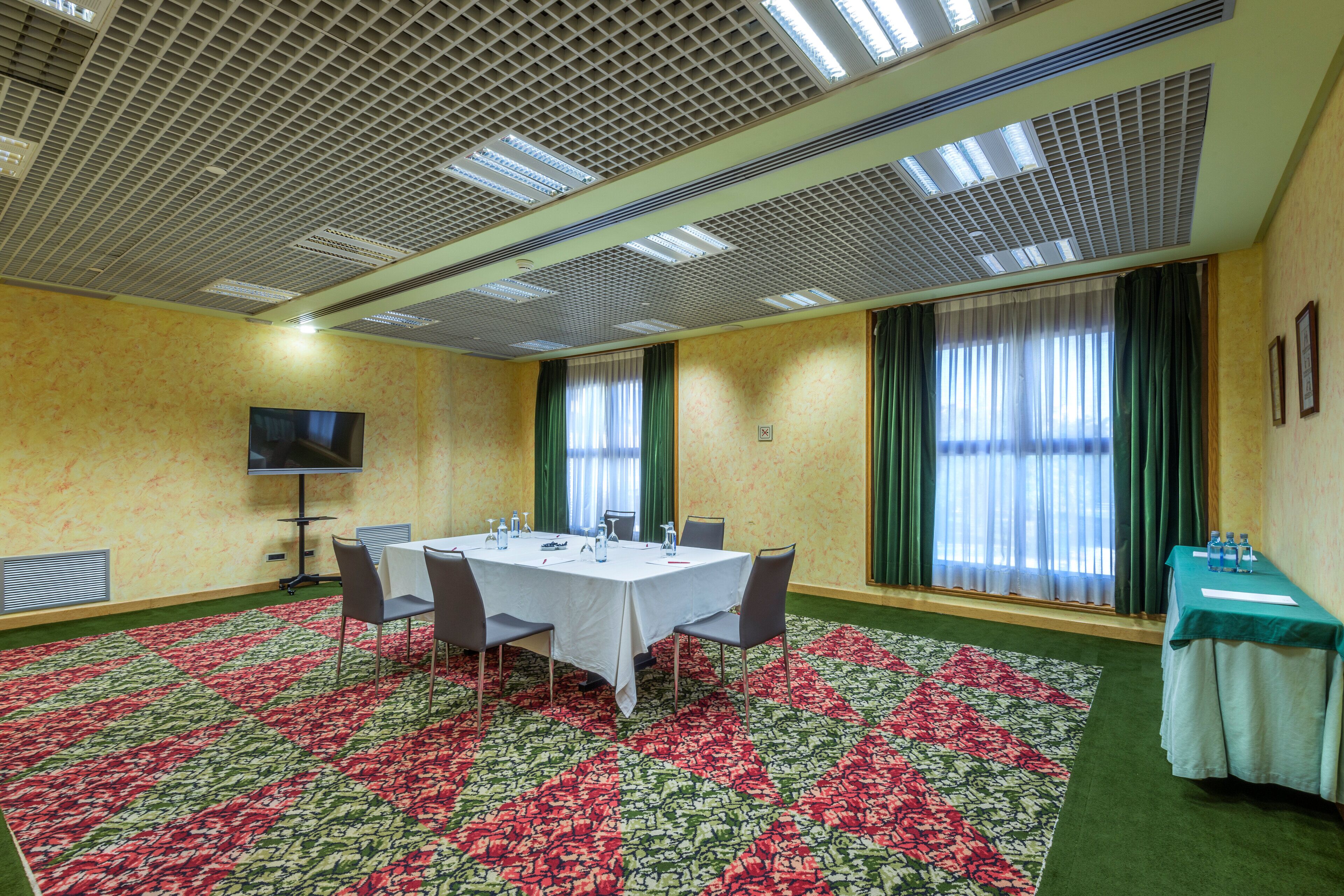 Una sala de conferencias con una gran mesa, sillas, un televisor de pantalla plana y piso alfombrado.
