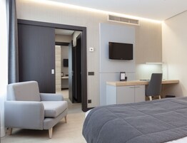 Una camera d'albergo con un letto, una scrivania con sedia, una televisione e una poltrona a fantasia.