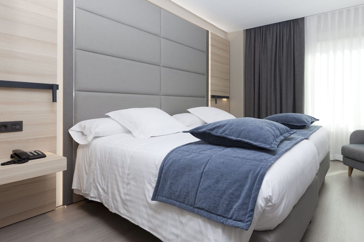 Moderni hotellihuone, jossa on suuri sänky, puhelin sängyn vieressä ja harmaa nojatuoli.