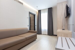 Una camera d'albergo moderna con divano, televisore a parete e parete decorativa in legno.