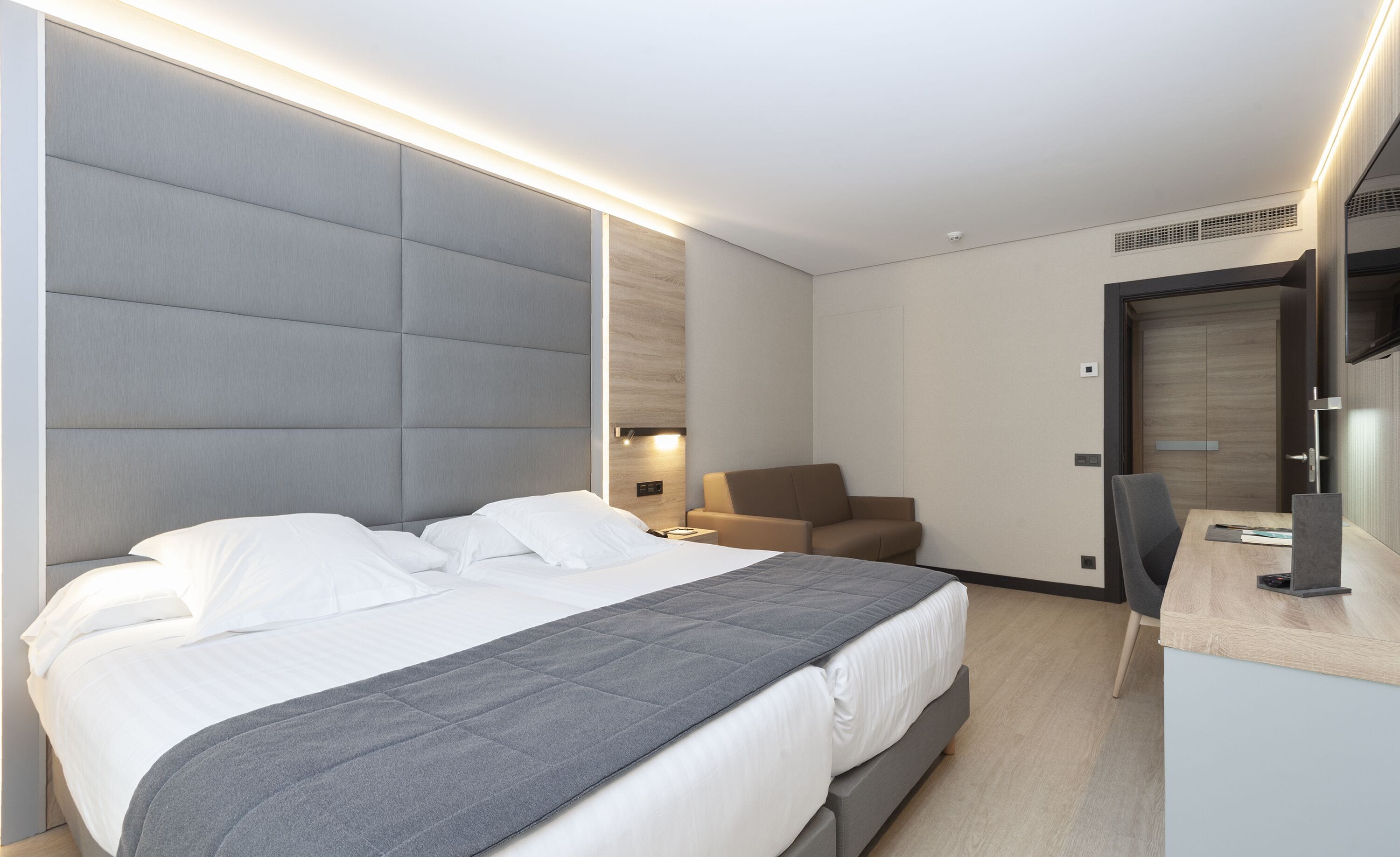 A modern hotel room with a large bed, a desk, and a chair.
