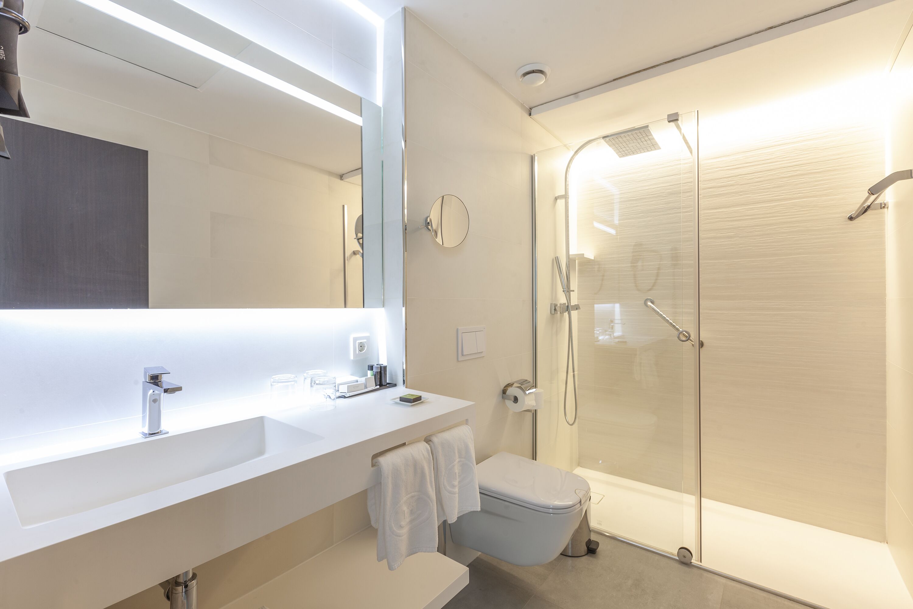 Un bany modern amb un lavabo blanc, mirall i plat de dutxa de vidre.