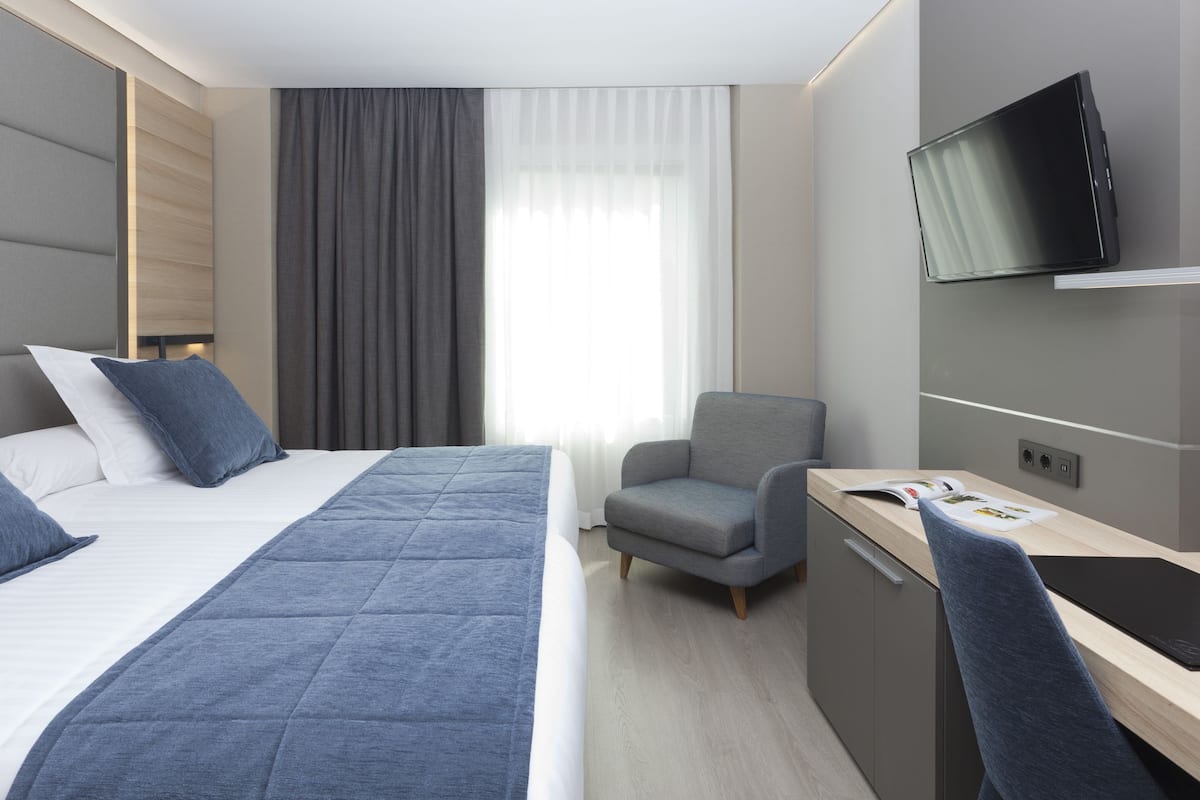 Moderni hotellihuone, jossa on suuri sänky, työpöytä, tuoli ja televisio.