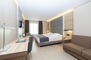 Ein modernes Hotelzimmer mit einem Bett, einem Schreibtisch, einem Sessel, einer Couch und einem Fernseher.