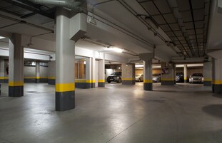 Un aparcamiento de varios niveles con pilares de hormigón y franjas amarillas, que muestra varios coches estacionados.