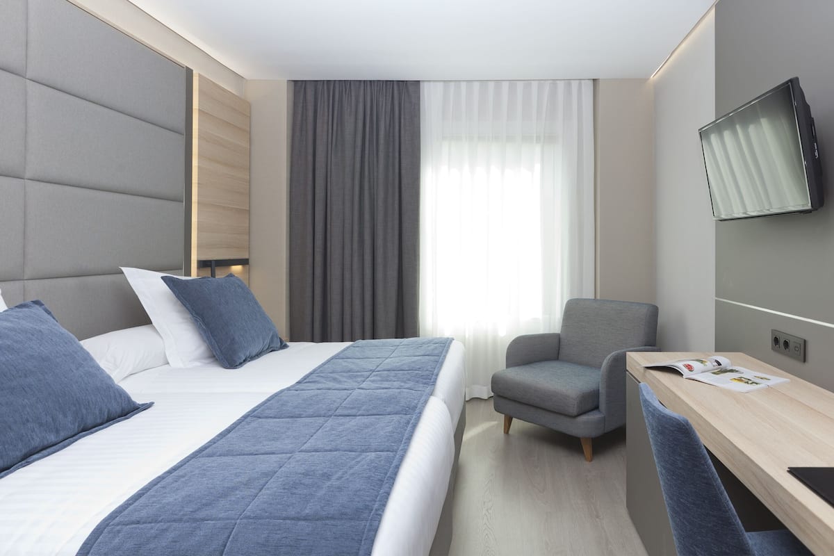 Moderni hotellihuone, jossa on suuri sänky, työpöytä ja seinälle asennettu televisio.