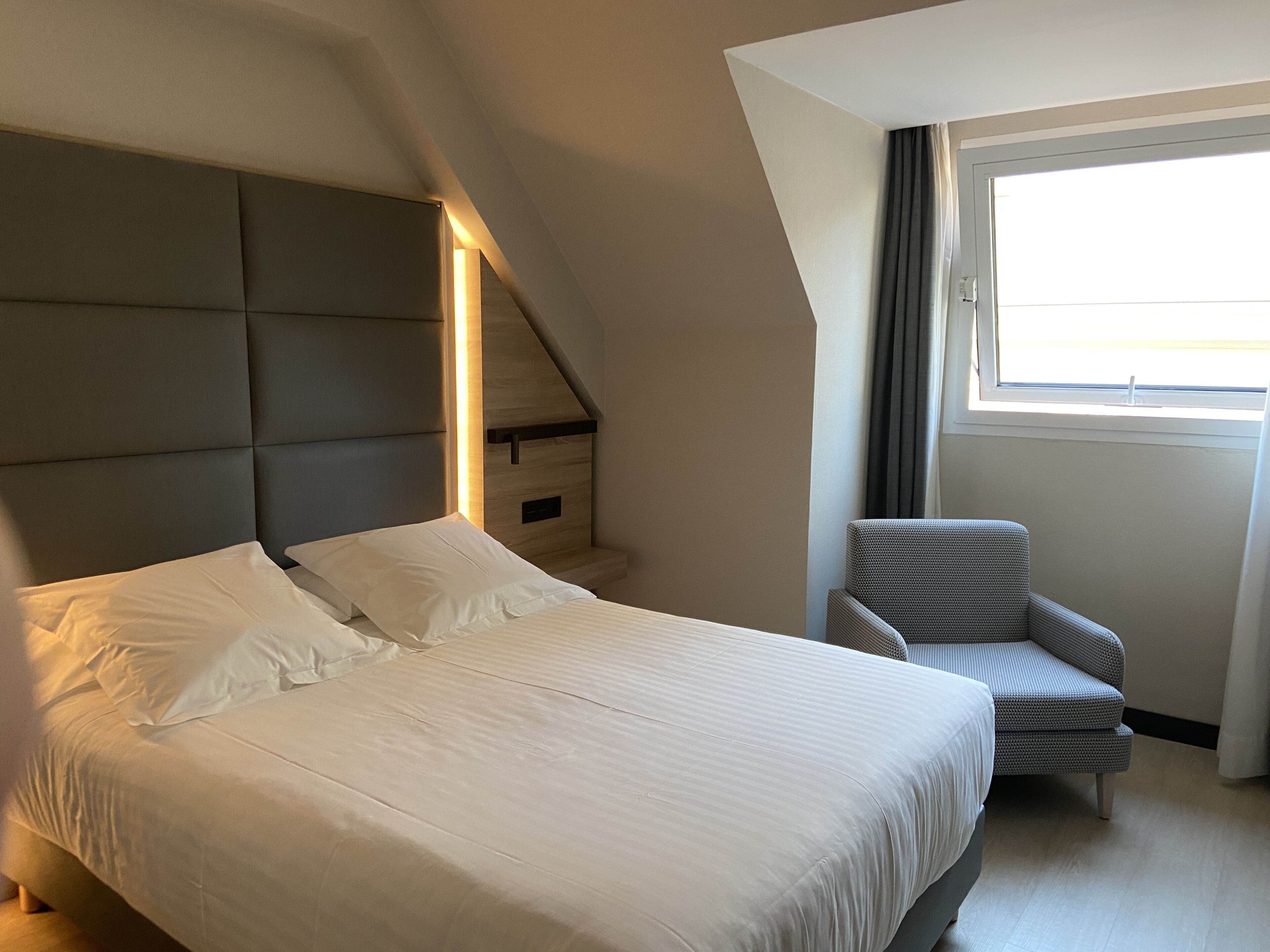 Una habitación de hotel moderna con una cama grande, una silla, una ventana y un techo inclinado.
