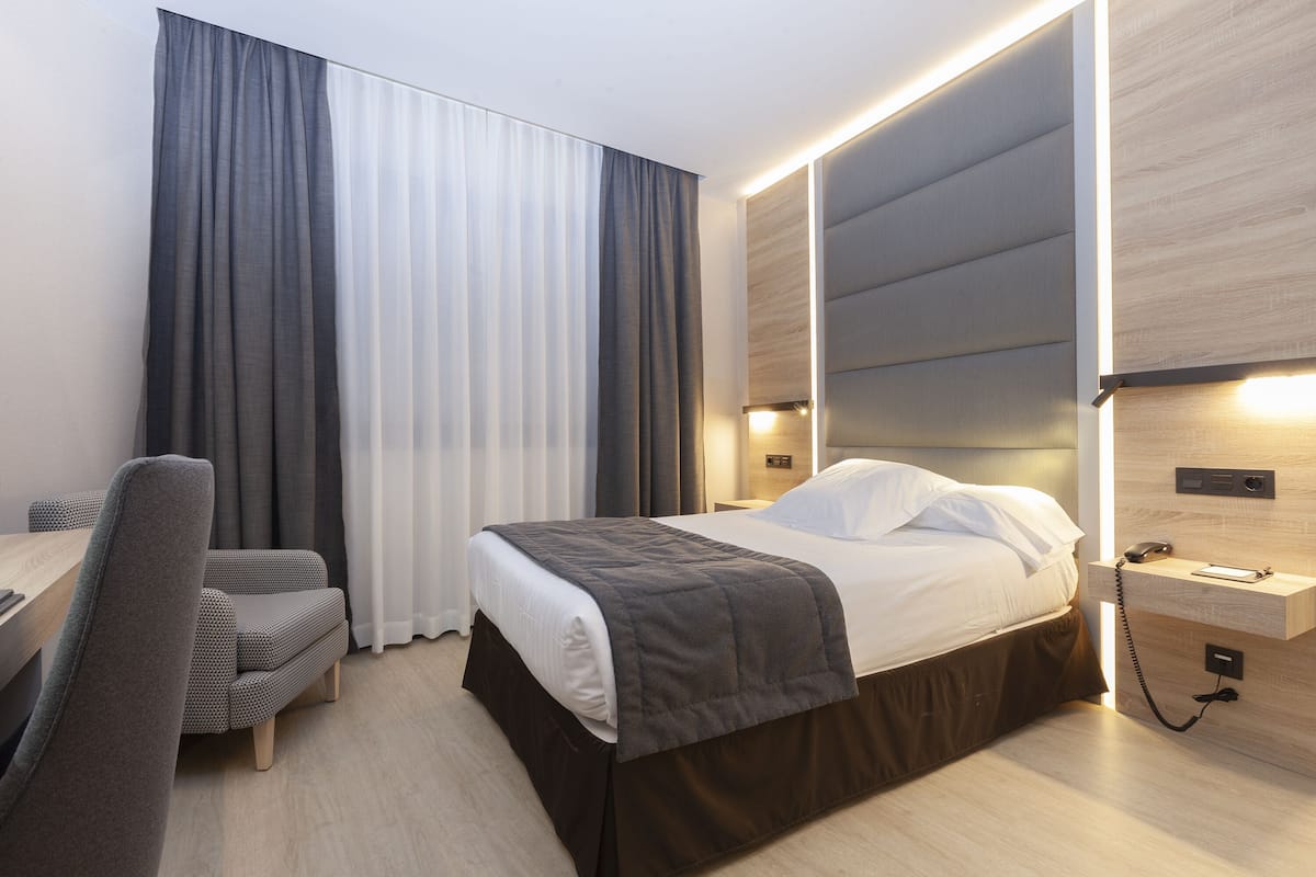 Moderni hotellihuone, jossa on sänky, yöpöytä ja työpöytä tuolilla.