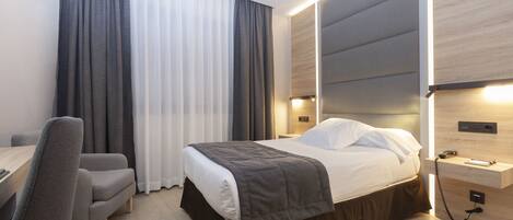 Ett modernt hotellrum med en säng, ett sängbord, en stol och ett skrivbord.
