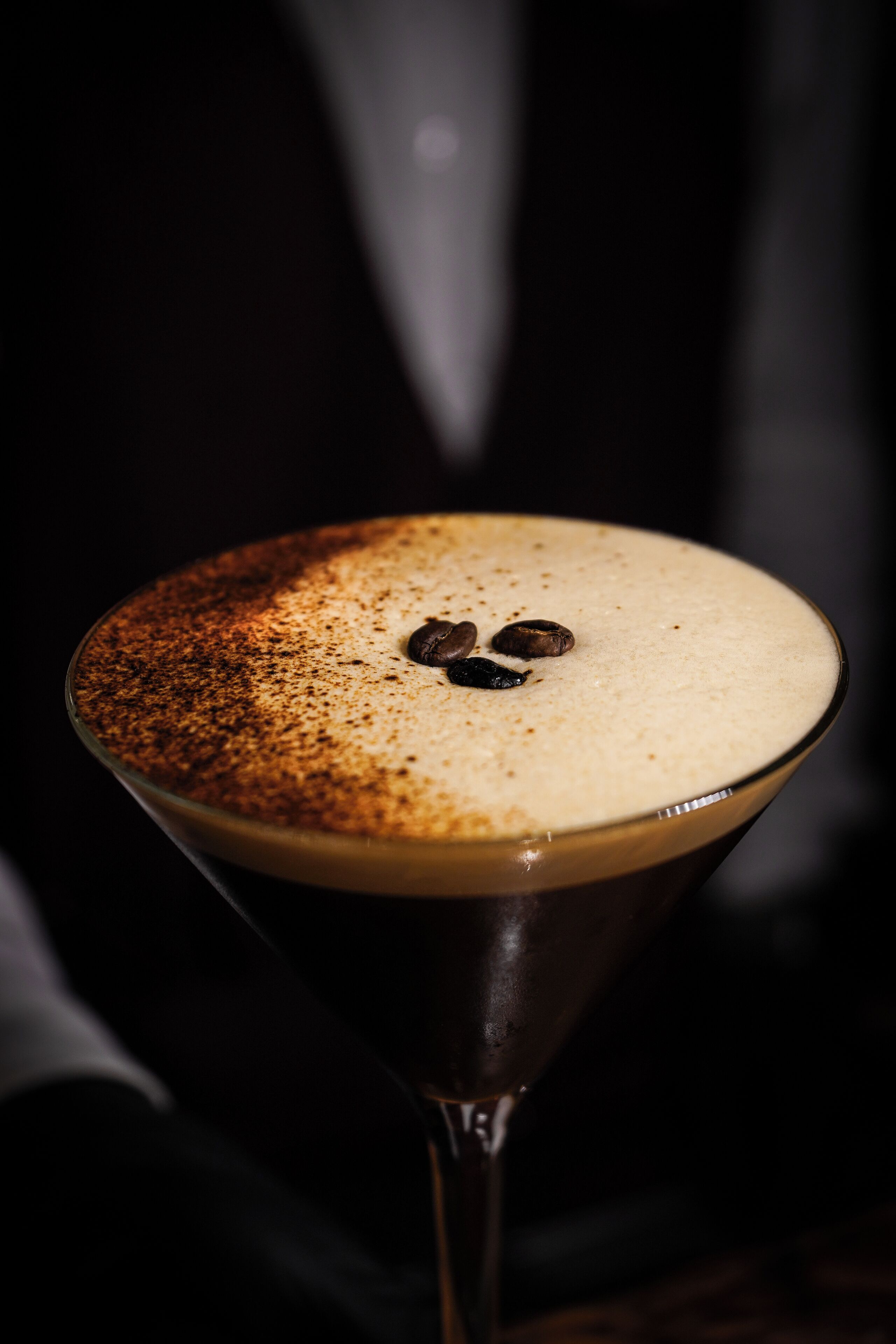 A martini glass with a frothy top and coffee beans on the rim.