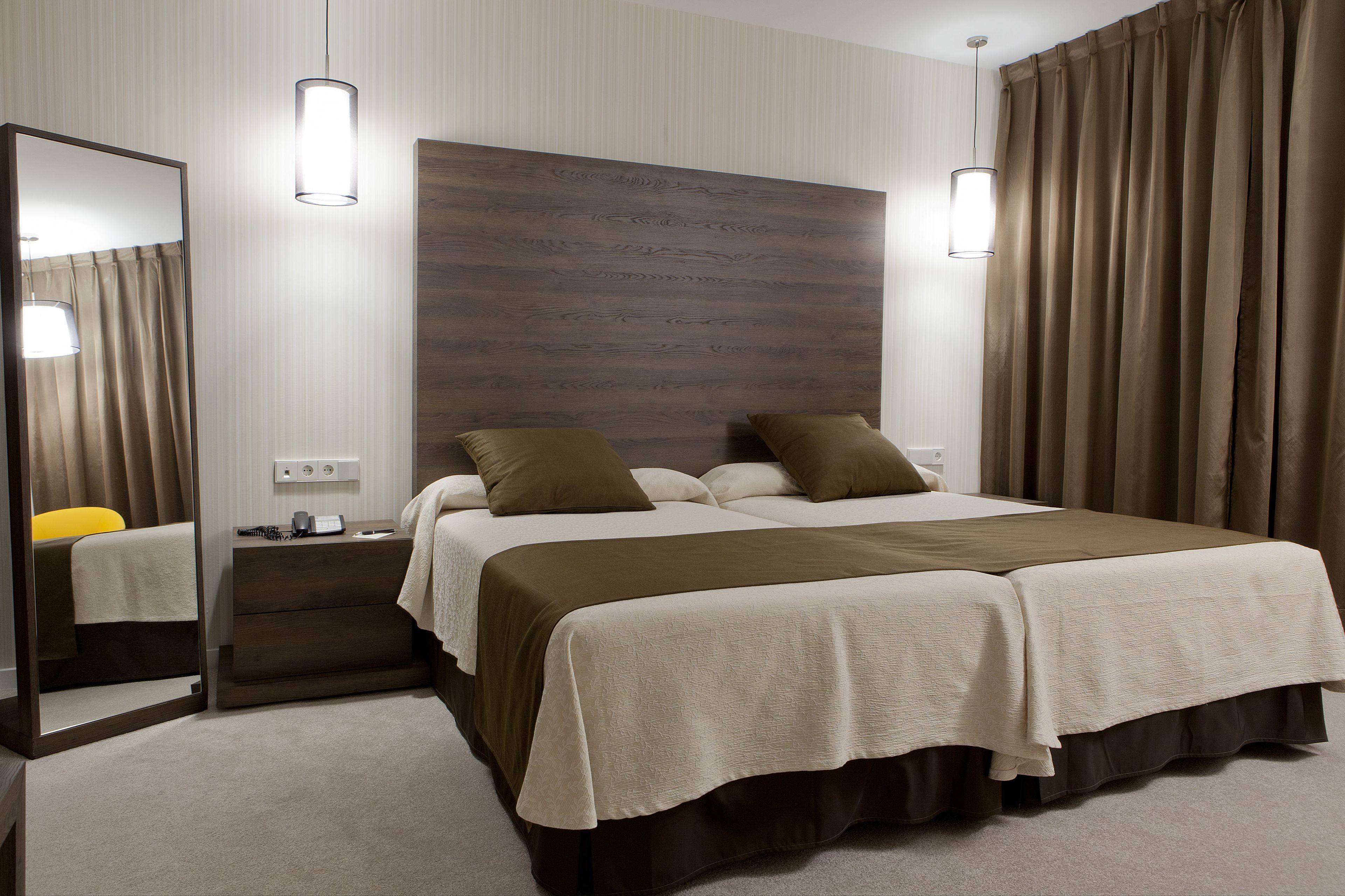 A double bed with a wooden headboard, a bedside table with a lamp, and a mirror.
