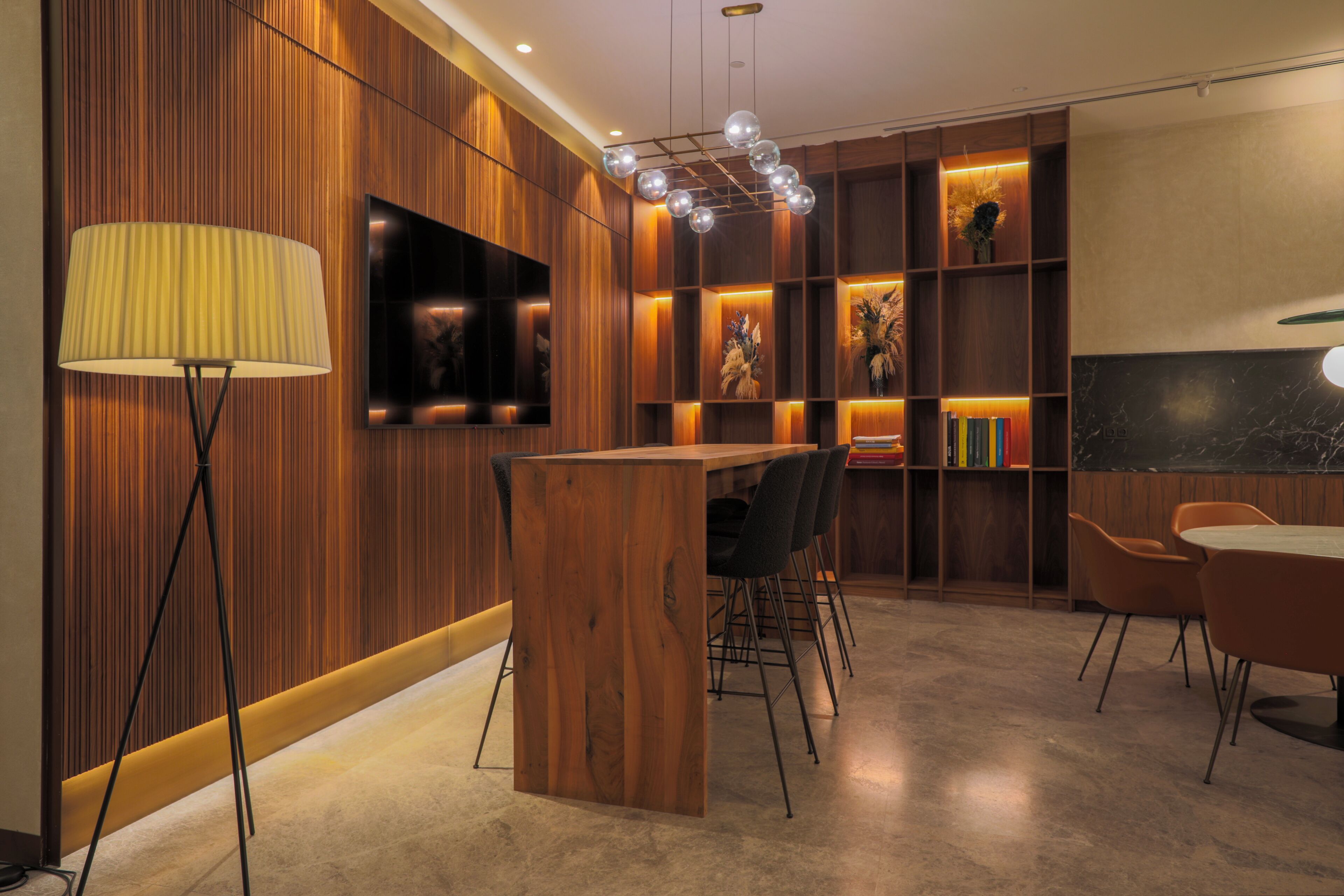 Un interior moderno con una pared de madera, un televisor montado en la pared, una mesa de madera con sillas y una estantería con libros y objetos decorativos.