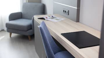 A modern room with a wooden desk, a grey armchair, and a small kitchenette.