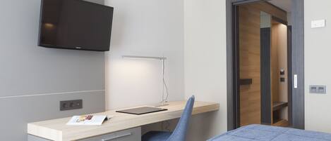 Una habitación de hotel moderna con una cama, un escritorio con una silla, un televisor de pantalla plana y una mesita de noche.