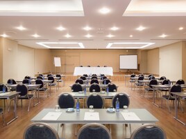 Un salón de conferencias con mesas, sillas, botellas de agua y una pizarra.