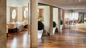 A modern hotel lobby with wooden flooring, a central seating area, and a dining section with tables and chairs. - Hotel Zentral Parque (Valladolid)