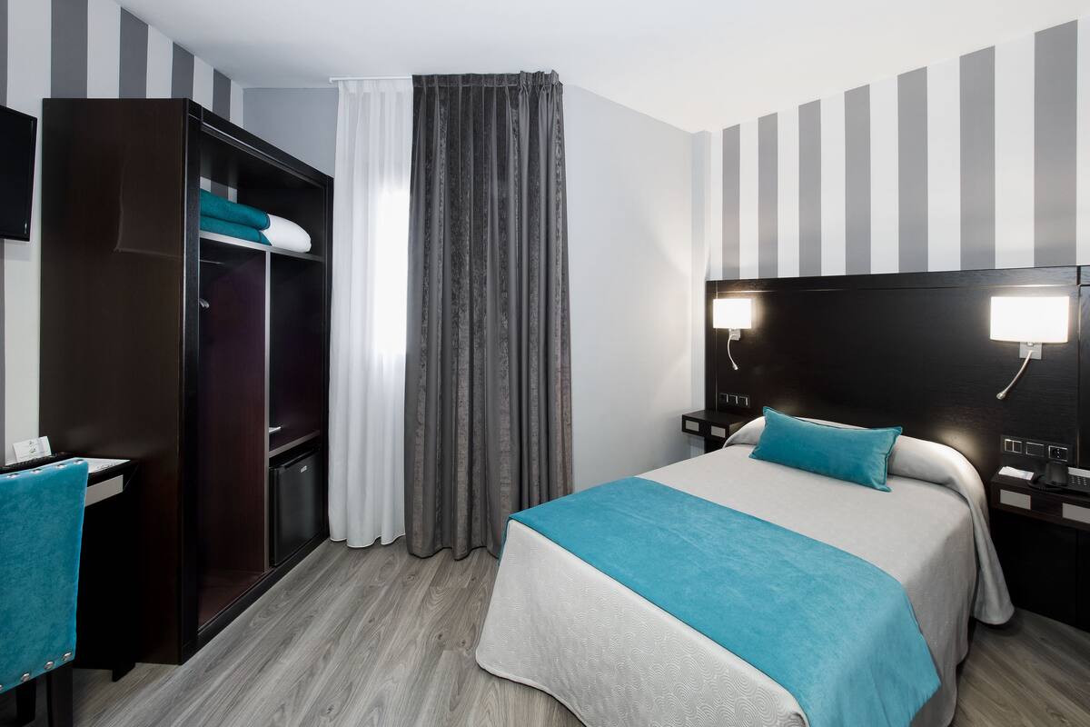 A hotel room with a bed, a desk, a wardrobe, and a TV.
