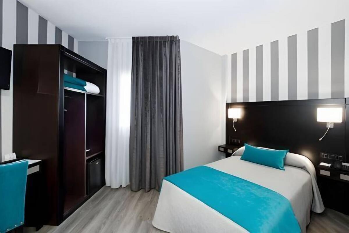 A hotel room with a bed, a wardrobe, a desk, and a curtain.