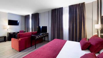 Ein Hotelzimmer mit einem großen Bett, einem roten Sofa, einem Schreibtisch mit Fernseher und Vorhängen.