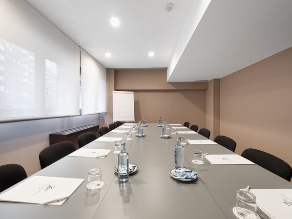 Un salón de conferencias con una larga mesa, sillas, una pizarra y una pantalla de proyector.