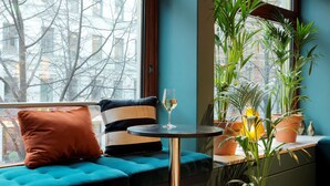 Ein modernes Zimmer mit einem salbeigrünem Sofa, einem kleinen runden Tisch und einem Glas Weißwein.