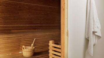 Una sauna de madera con un banco de madera, un cubo de madera con una cuchara y una toalla blanca colgada de un gancho.