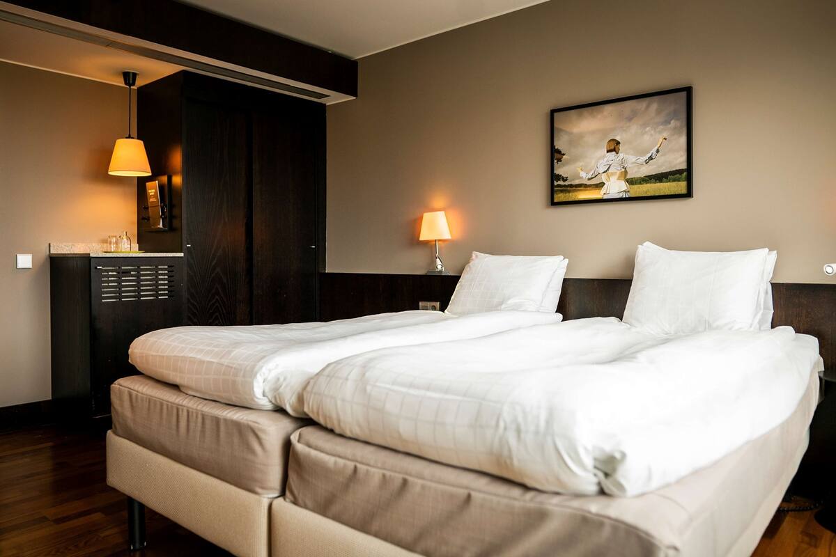 Ein Hotelzimmer mit einem Doppelbett, zwei Nachttischen, einer Lampe, einem Bild und einer Minibar.