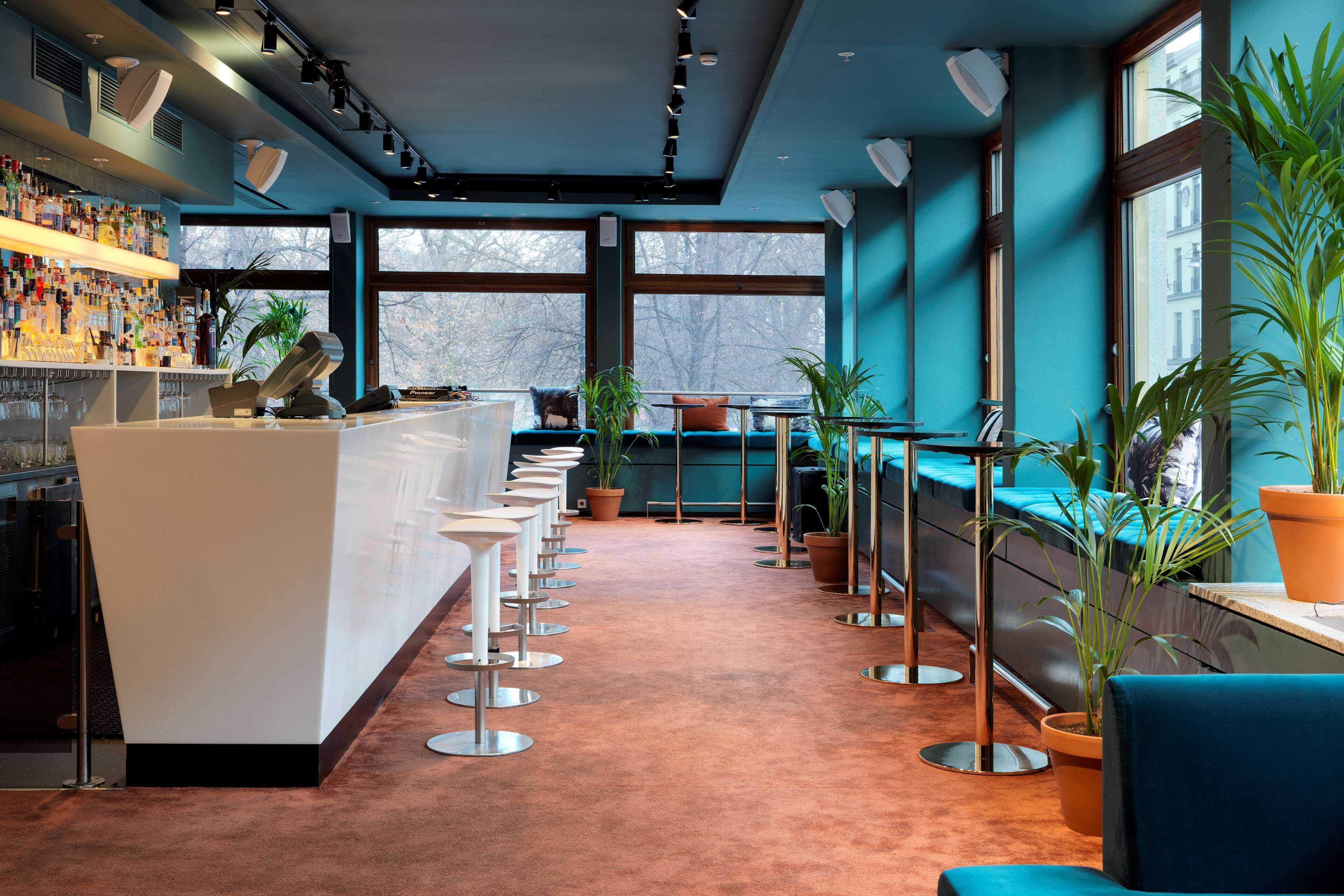 A bar area with a long counter, multiple stools, and potted plants.
