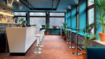 A bar area with a long counter, multiple stools, and potted plants.