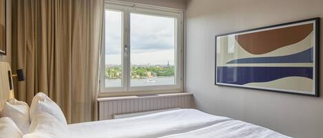 Una camera d'hotel con un letto grande, una finestra vista sulla città e un quadro appeso al muro.